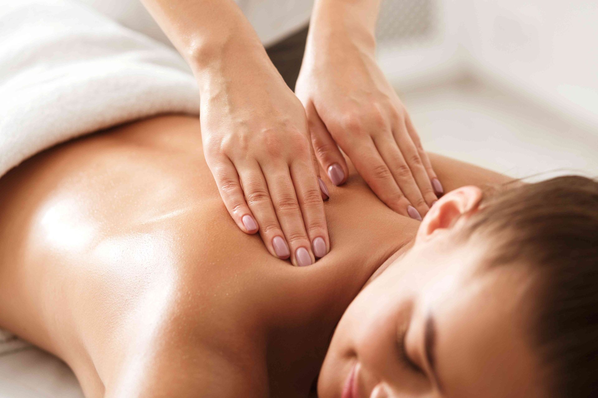 Person receiving a massage with hands applying pressure to the back in a relaxing setting.