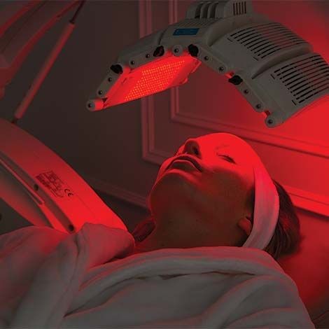 Patient undergoing a red light therapy treatment, illuminated by a specialized machine emitting red LED light.